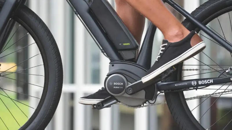 Foto mit Zoom auf den Bosch-Motor eines E-Bikes, auf dem Pedal Füße in Canvasschuhen Foto mit Zoom auf den Bosch-Motor eines E-Bikes, auf dem Pedal Füße in Canvasschuhen